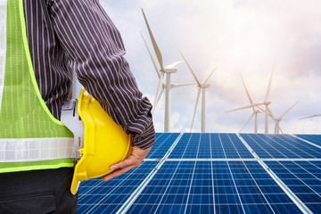 Young business man engineer hold yellow helmet at solar panel and wind generators power plant construction site background