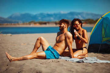 Wall Mural - Young woman applying sun lotion to a man on the back