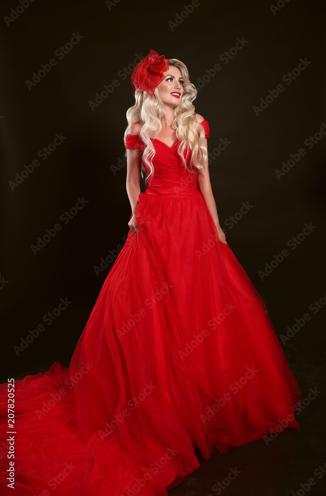 Blonde woman in red dress and elegant hat isolated on studio black  background. Beautiful blond girk with long wavy hair posing in prom gown.  Stock Photo | Adobe Stock