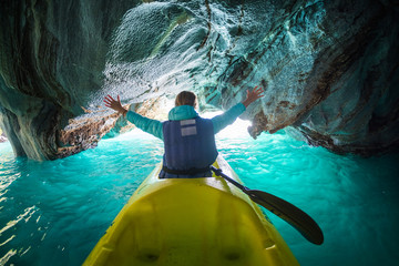 Wall Mural - Woman sits in kayak with rised hands inside the Marble Cave on the lake of General Carrera, Chile