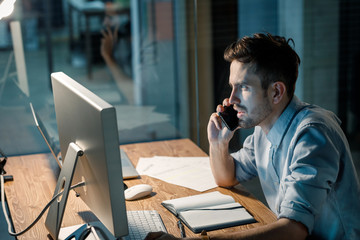 Wall Mural - Casual man watching computer working overhours and having phone call late at night. 