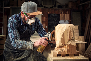 A young man carpenter in a suit, goggles   saws a man's head with a tree , using an angle grinder  in the workshop, around a lot of tools for work