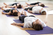 © fizkes - Group of young sporty people practicing yoga lesson, doing Savasana, Dead Body pose, Corpse exercise, working out, indoor full length, students training in sport club, studio