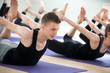 © fizkes - Yogi man and a group of young sporty people practicing yoga lesson, doing Bow pose, Dhanurasana exercise, working out, indoor close up, students training in sport club. Wellness, lifestyle concept