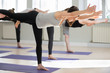 © fizkes - Group of young sporty people practicing yoga, doing Warrior three exercise, Virabhadrasana 3 pose, indoor close up, yogi students working out in sport club, studio. Active lifestyle, wellness concept