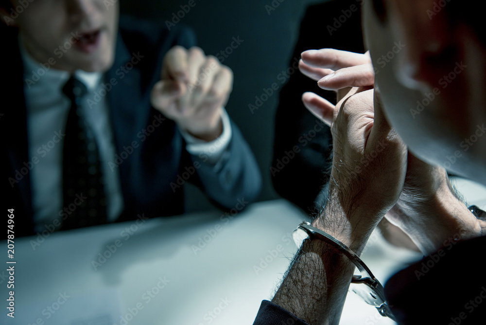 Criminal man with handcuffs being interviewed in interrogation room - obrazy, fototapety, plakaty 