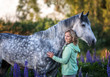 Woman with a grey horse outdoors.