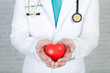 © jayzynism - Young man doctor holding a red heart, standing on wall background.