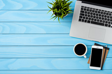 Office desktop with modern laptop on blue wooden background. Top view