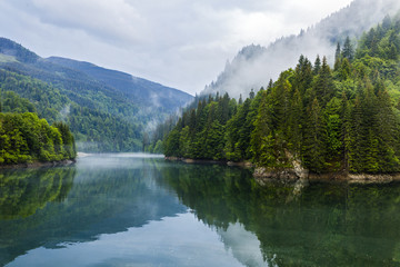 Landscape with lake and misty forest in mountains in a rainy day