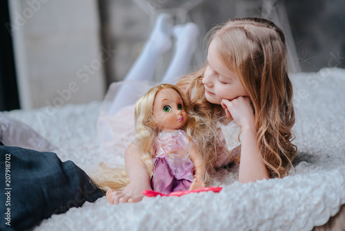 Photographie Adorable toddler girl with blond curly hair playing indoors with doll