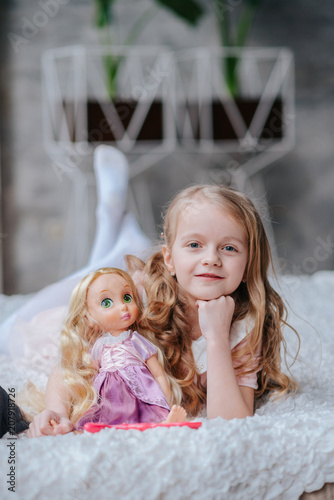 Adorable toddler girl with blond curly hair playing indoors with doll Poster Mural XXL