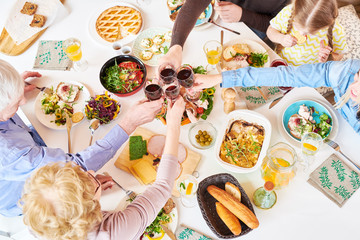 Top view of big happy family sitting at dinner table enjoying delicious homemade food and toasting during festive celebration