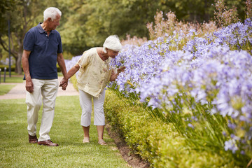 Senior Couple Holding Smelling Flowers On Walk In Park Together