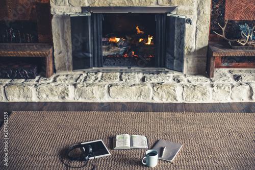 Cuadros en Lienzo Wide shot of open Bible, coffee, notepad and tablet in front of fire place