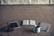 Photo of open Bible, coffee, notepad and tablet on a rug