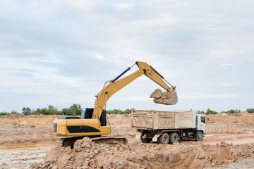 Wall Mural - Yellow excavator machine loading soil into a dump truck at construction site