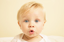 Close Up Portrait Of Cute Baby With Blonde Hair Looking Surprised In His Crib