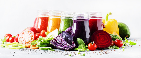 Food and drinks, selection of healthy and useful colorful vegetable juices and smoothies with chia and flax seeds in glass bottles, set on gray background, selective focus