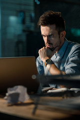 Wall Mural - Pensive and frowning man trying to solve problem at work watching laptop at table