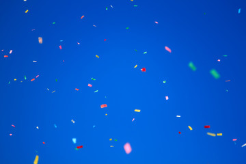 multicolored confetti on clear blue sky background. Concept of holiday backdrop