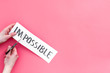 © 9dreamstudio - All is possible concept. Hands cutting the part im of written word impossible by sciccors. Pink background top view copy space