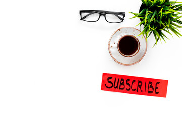 Poster - Email subscribe concept. Hand lettering subcribe on work desk with plant, glasses, cup of coffee on white background top view copy space