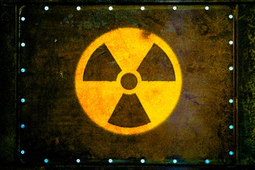 Wall Mural - Round yellow radioactive (ionizing radiation) danger warning symbol painted on massive rusty metal plate fixed with metallic rivets to the wall with dark rusty brown and green moss.