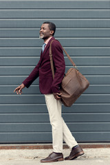 Wall Mural - stylish mature african american man posing in trendy burgundy jacket with leather bag