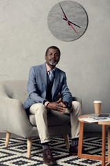 Wall Mural - confident african american businessman sitting at table with newspaper, coffee and laptop