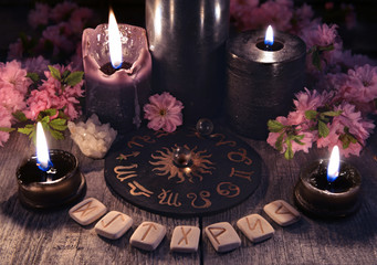 Wall Mural - Runes, black candles and zodiac circle against the background with sakura flowers. Occult, esoteric and divination still life. Halloween background with vintage objects