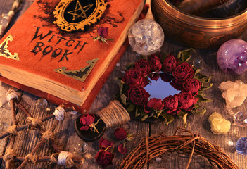 Witch book with magic rose mirror, pentagram and mystic objects on planks. Occult, esoteric and divination still life. Halloween background with vintage objects 