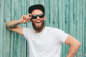 Hipster handsome male model with beard wearing white blank t-shirt and a baseball cap with space for your logo or design in casual urban style