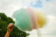 The hand of women holding coloured  cotton candy in the background of the blue sky and green tree