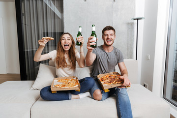 Canvas Print - Cheerful young couple eating pizza and drinking beer