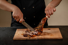 Chef Is Cutting Roasted Leg Lamb On Wooden Board On Table