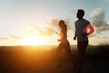 Two Athletes Running At Sunset. Backlit Silhouette Of Man And Woman Training Together.