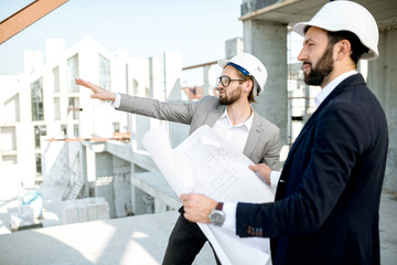 Two business men or engeneers working with house drawings on the structure during the construction process outdoors