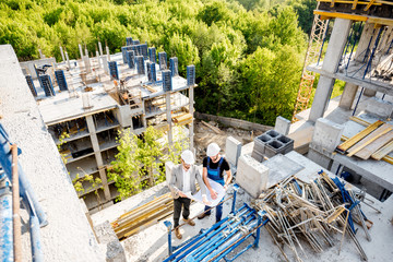 Top view on the construction site of residential buildings during the construction process with two workers standing with drawings