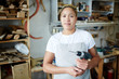 © pressmaster - Female woodworker holding drill and looking at camera while standing in workshop.