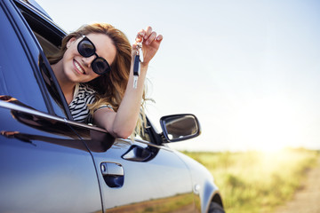 An attractive woman in a car holds a car key in her hand.