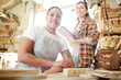 © pressmaster - Two women smiling and looking at camera while working in nice carpenter workshop together.