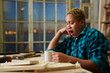 © pressmaster - Exhausted female woodworker holding mug with hot drink and yawning while sitting near workbench in workshop in evening.