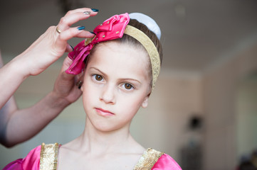 mother hands correct hat of young cute russian dancer ballerina girl indoors