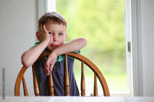 Fotografie, Obraz bored kid holding hand on cheek. the boy leaning on a chair