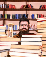 Leinwandbilder - Time flow concept. Teacher or student with beard studying in library. Man, scientist in glasses looks at hourglass. Man on serious face watching time is going over, bookshelves on background.