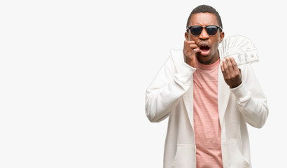 Wall Mural - African man holding dollar bank notes terrified and nervous expressing anxiety and panic gesture, overwhelmed