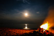 Long exposure of a full moon with bonfire on a sandy beach and ocean in the background, Khanom Beach, Thailand