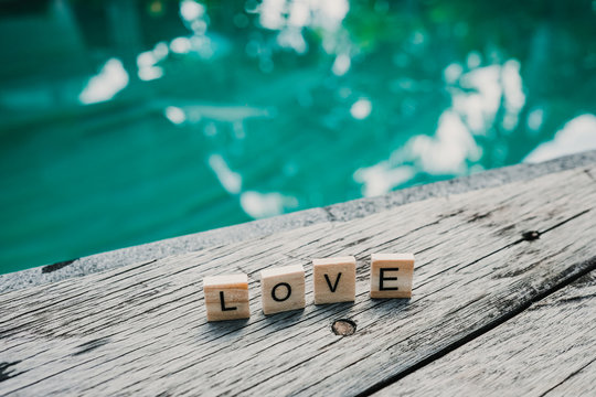 .Small wooden letters forming the word love on the edge of a pool with crystal blue water. Love concept. Lifestyle
