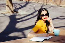 Portrait Of A Smiling Woman With Sunglasses Writing In A Notebook In The Park